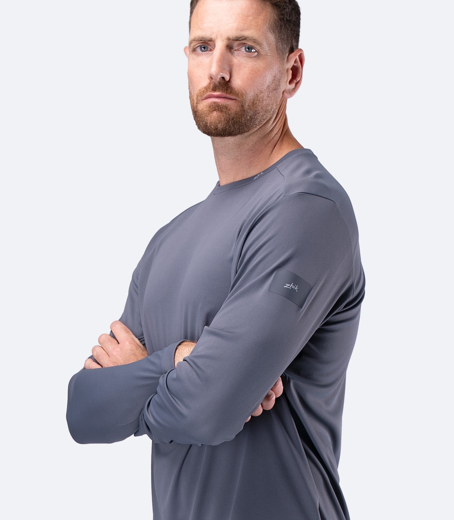 Side profile of Zhik Men's UVActive Long Sleeve Tech Top in Slate, arms crossed, showing clean teamwear styling