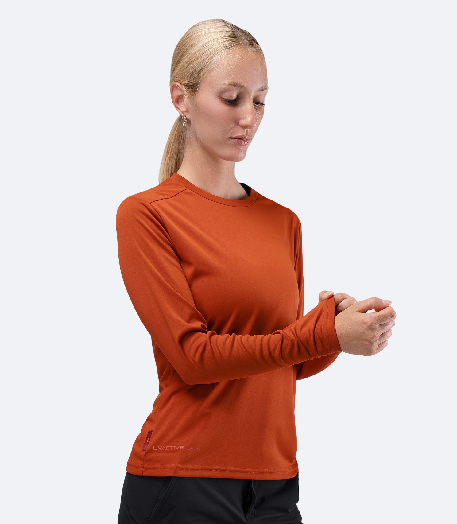 Front view of Women's Zhik UVActive long sleeve tech top in Red Earth, hand on sleeve showing UPF 50+ coverage