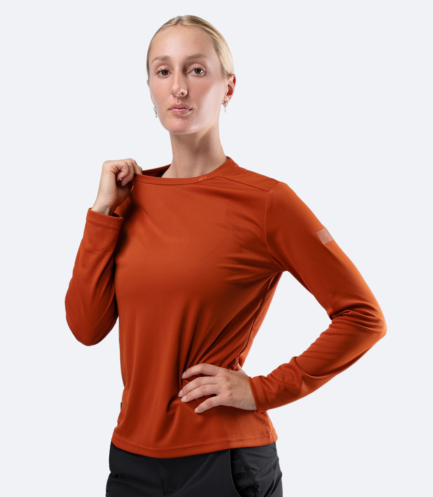 Front view Women's Zhik UVActive long sleeve tech top in Red Earth, hand on collar showing soft stretch neckline