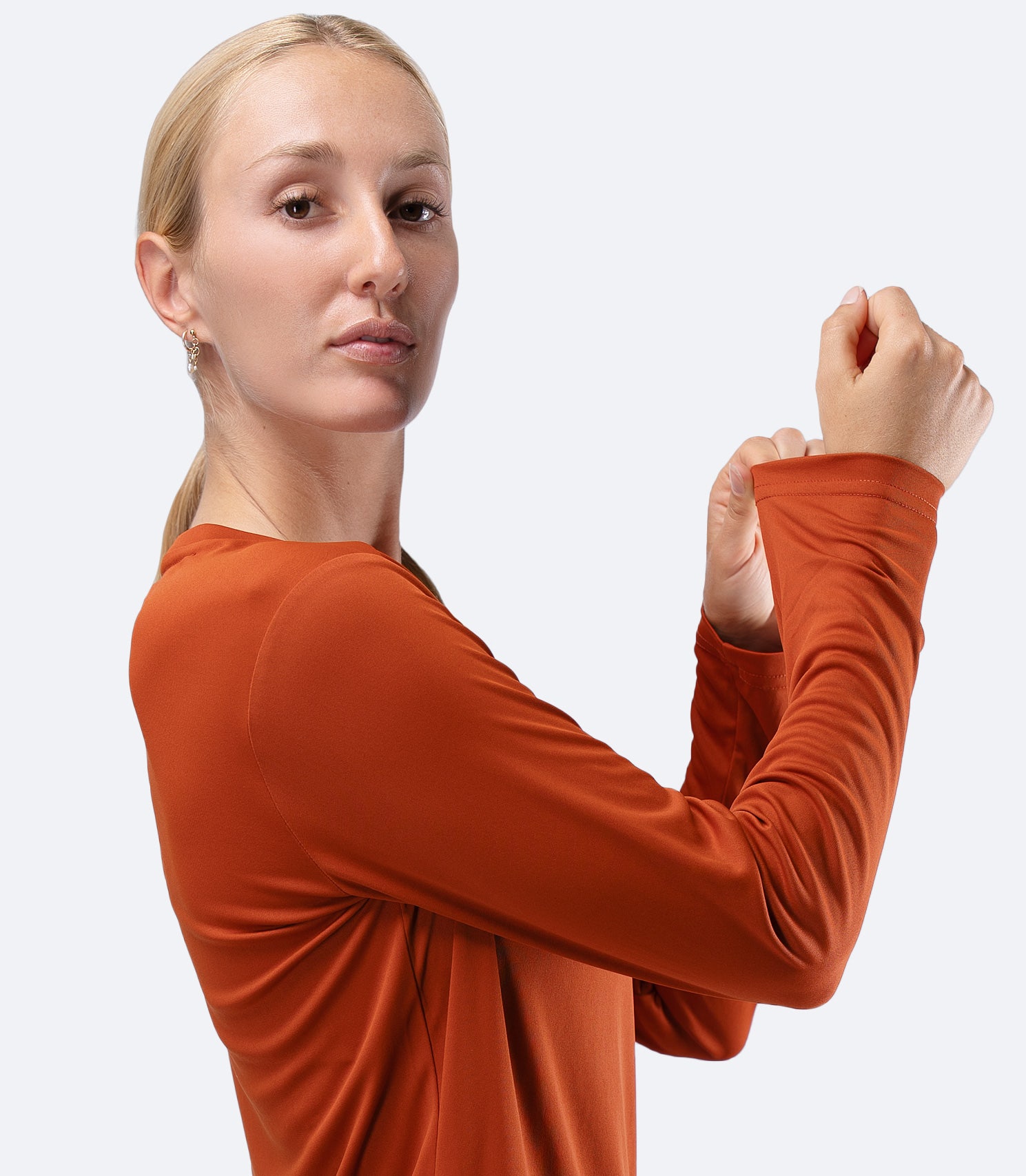 Close-up side arm of Women's Zhik UVActive top in Red Earth, wrist stretching sleeve to show flexible UPF fabric