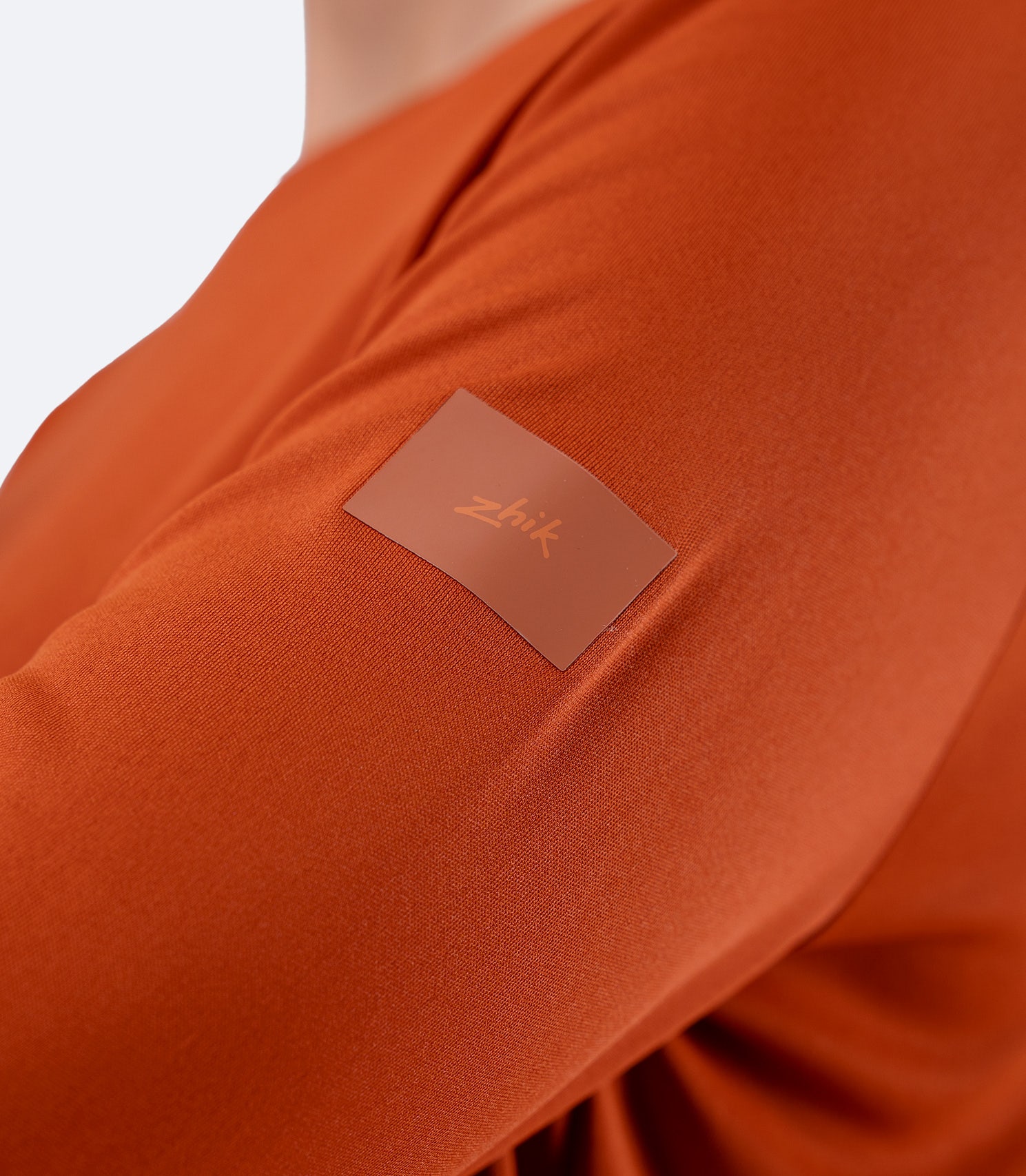 Close-up shoulder of Women's Zhik UVActive top in Red Earth, showing subtle Zhik logo and smooth knit finish