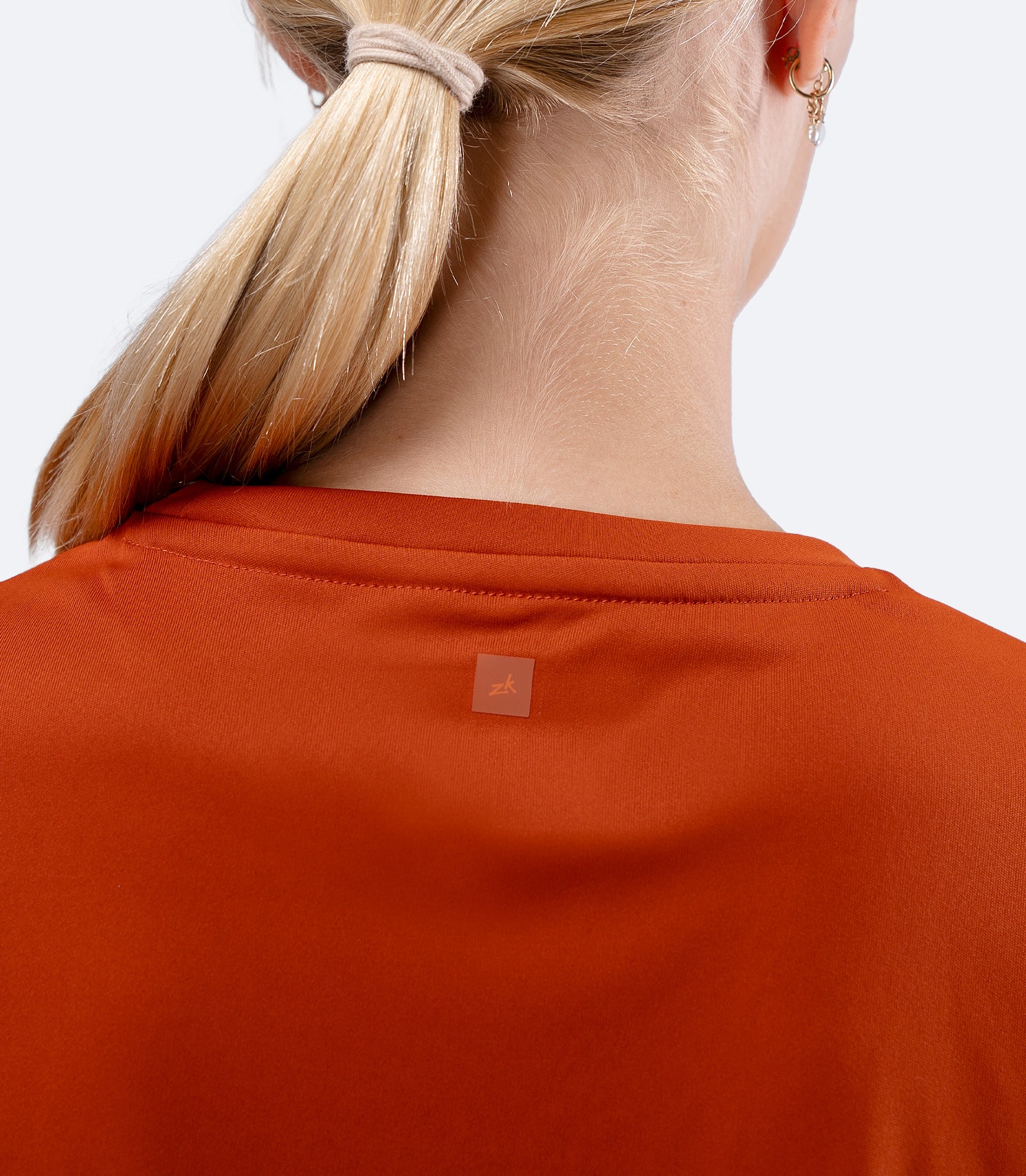 Back shoulder view of Women's Zhik UVActive top in Red Earth, with subtle Zhik logo between shoulder blades