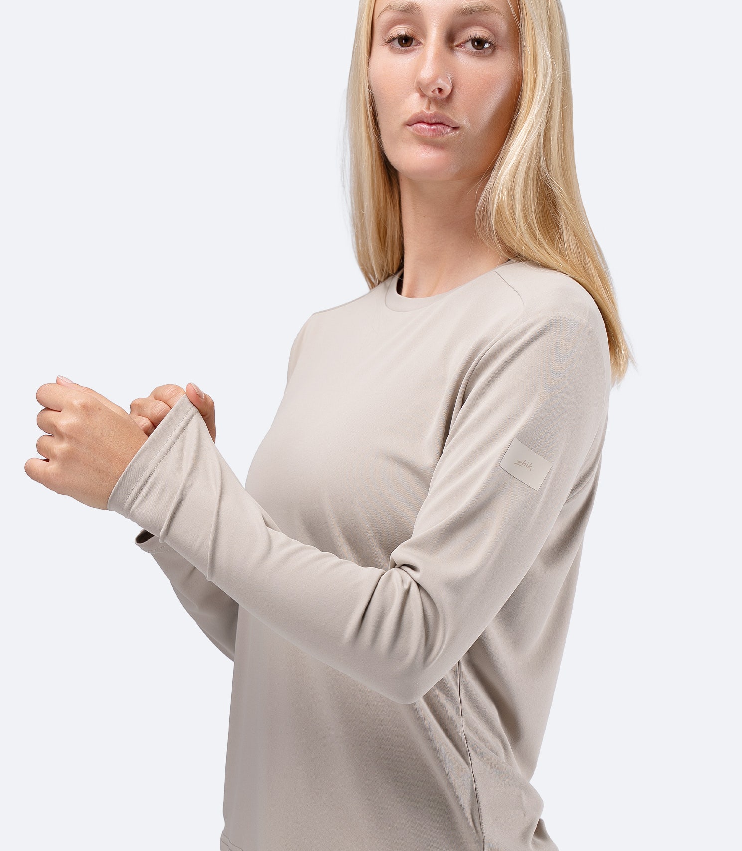 Front view of Women's Zhik UVActive long sleeve tech top in Stone, hand on sleeve showing UPF 50+ coverage
