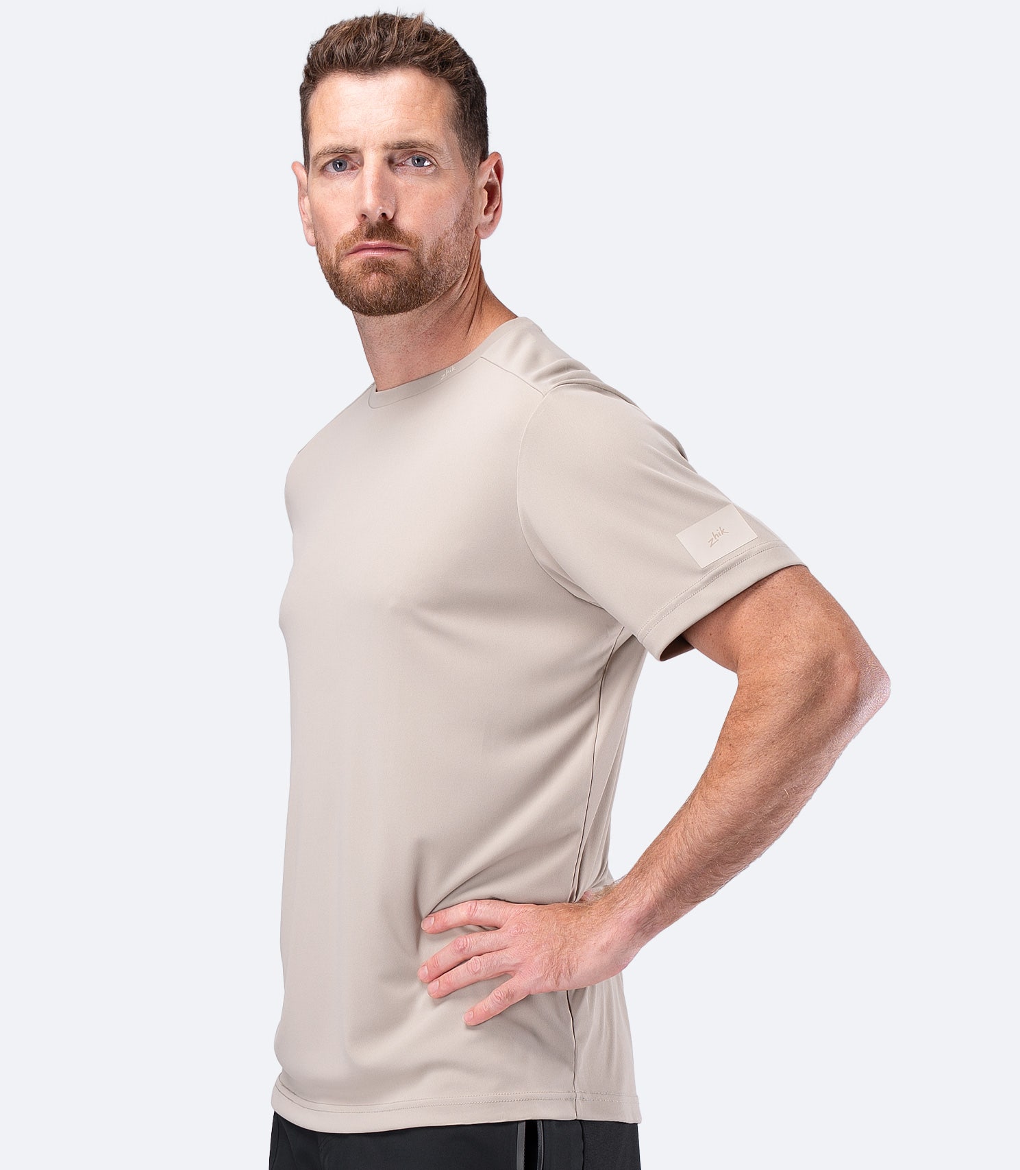 Side profile of Zhik Men's UVActive Tech Tee in Stone, one hand on hip highlighting relaxed sports fit