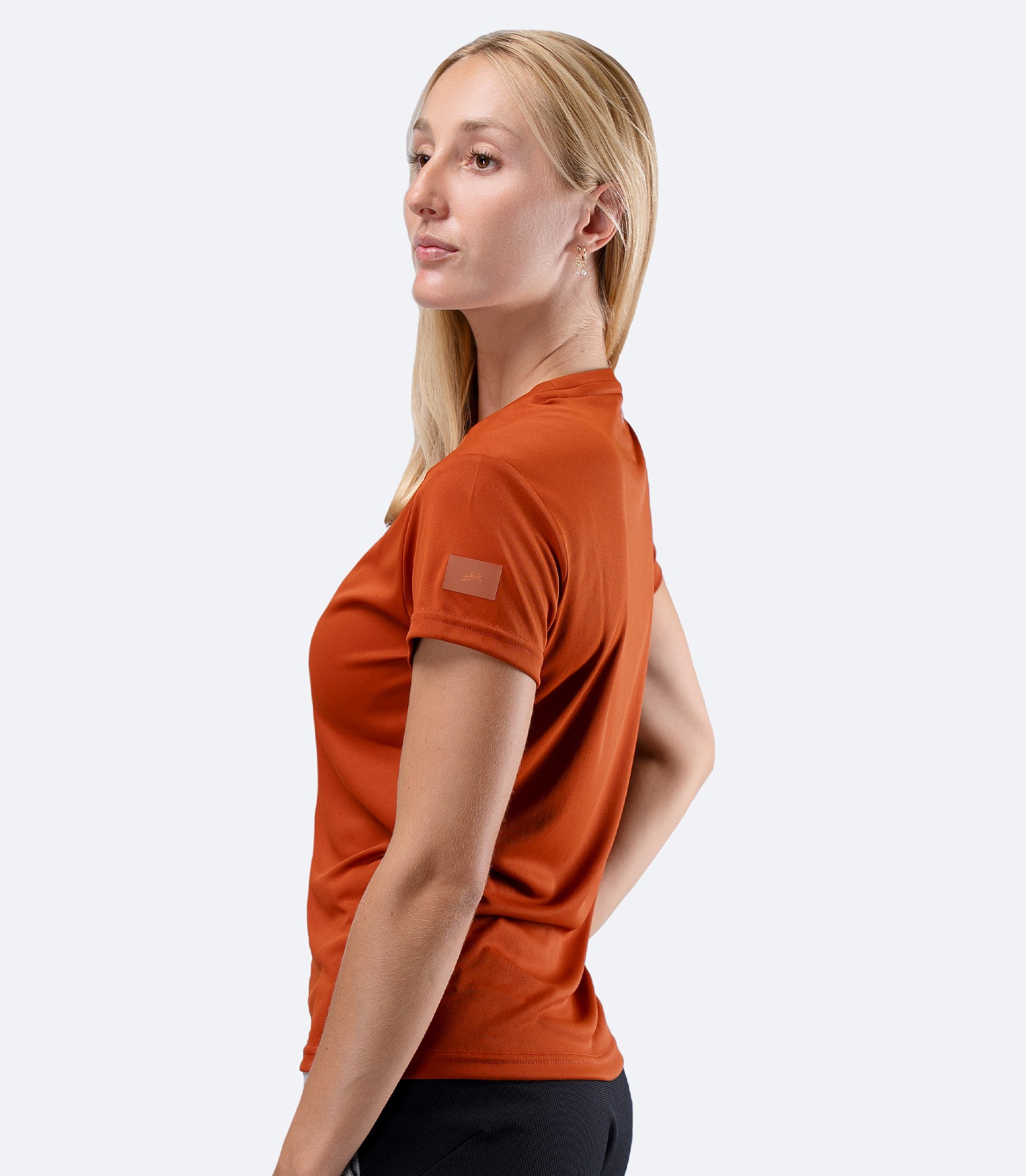 Zhik Women's UVActive short sleeve tech tee in Red Earth, side profile with one hand on hip