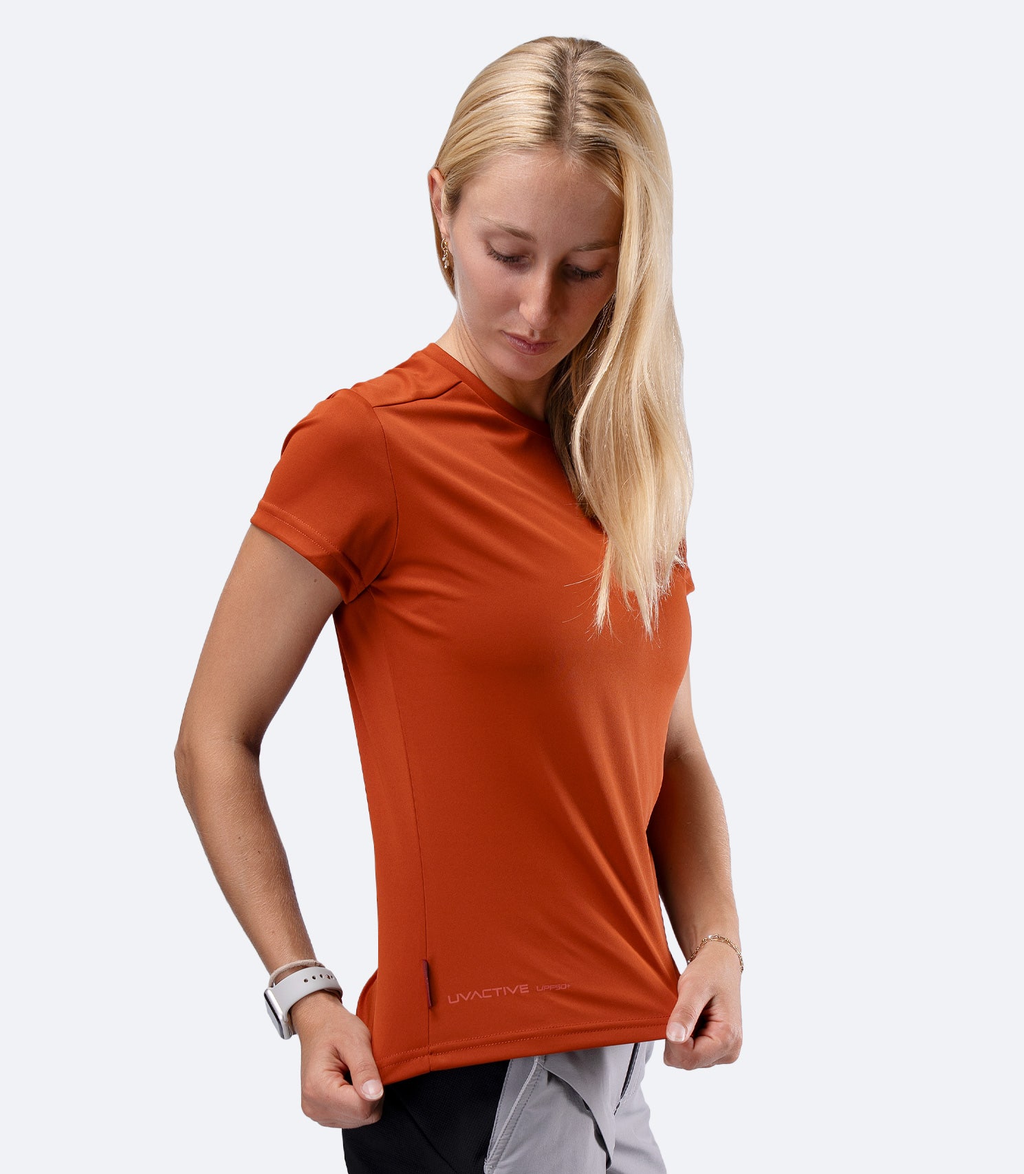 Zhik Women's UVActive short sleeve tech tee in Red Earth, side profile with hands on waist stretching fabric