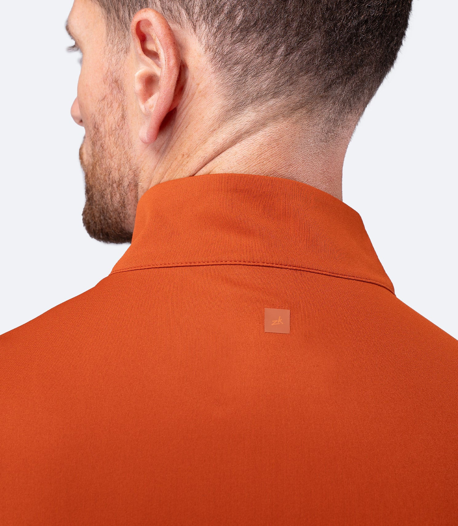 Back shoulder view of Zhik Men's UVActive Top in Red Earth, subtle Zhik logo between shoulder blades.