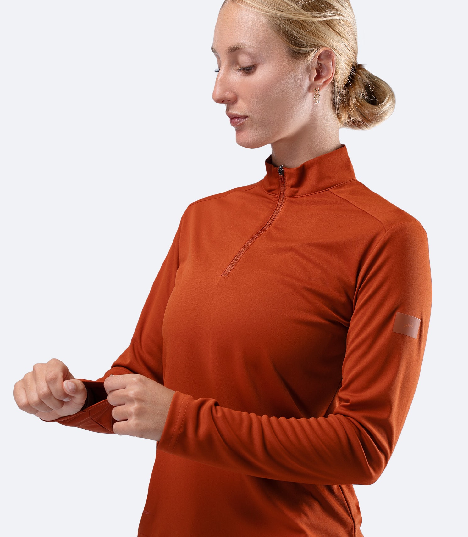 Zhik Women's UVActive 1/4 Zip Top in Red Earth, front view with hand on sleeve showing relaxed regular fit