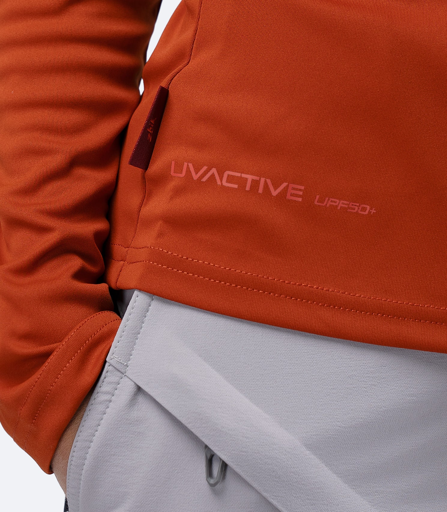 Close-up of UVActive UPF50+ logo and subtle Zhik tag at waistline on Red Earth Women's Tech Top