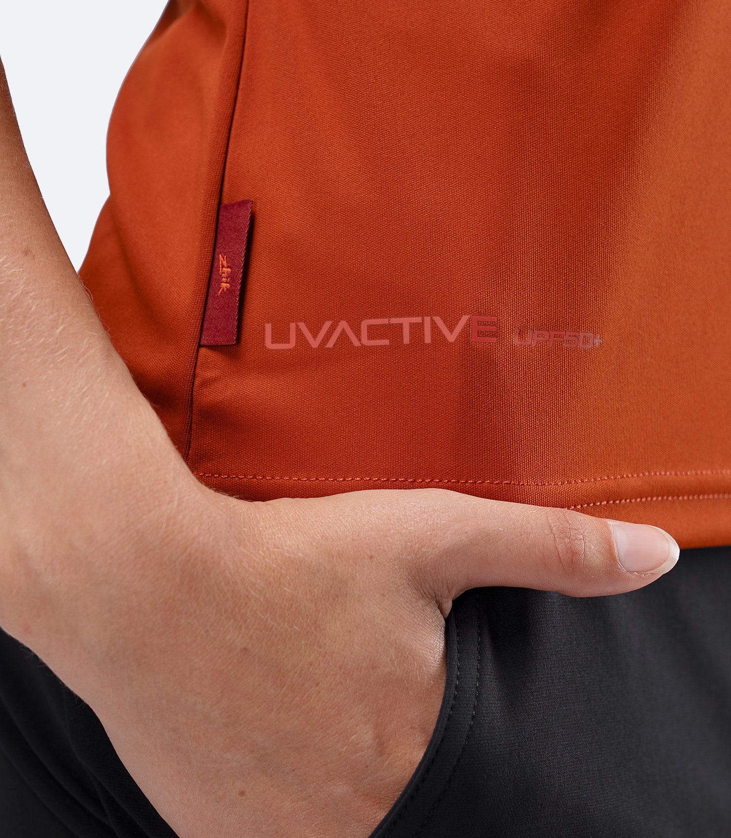 Close-up UVACTIVE UPF50+ logo on Red Earth Zhik Polo, with subtle Zhik tag at waistline