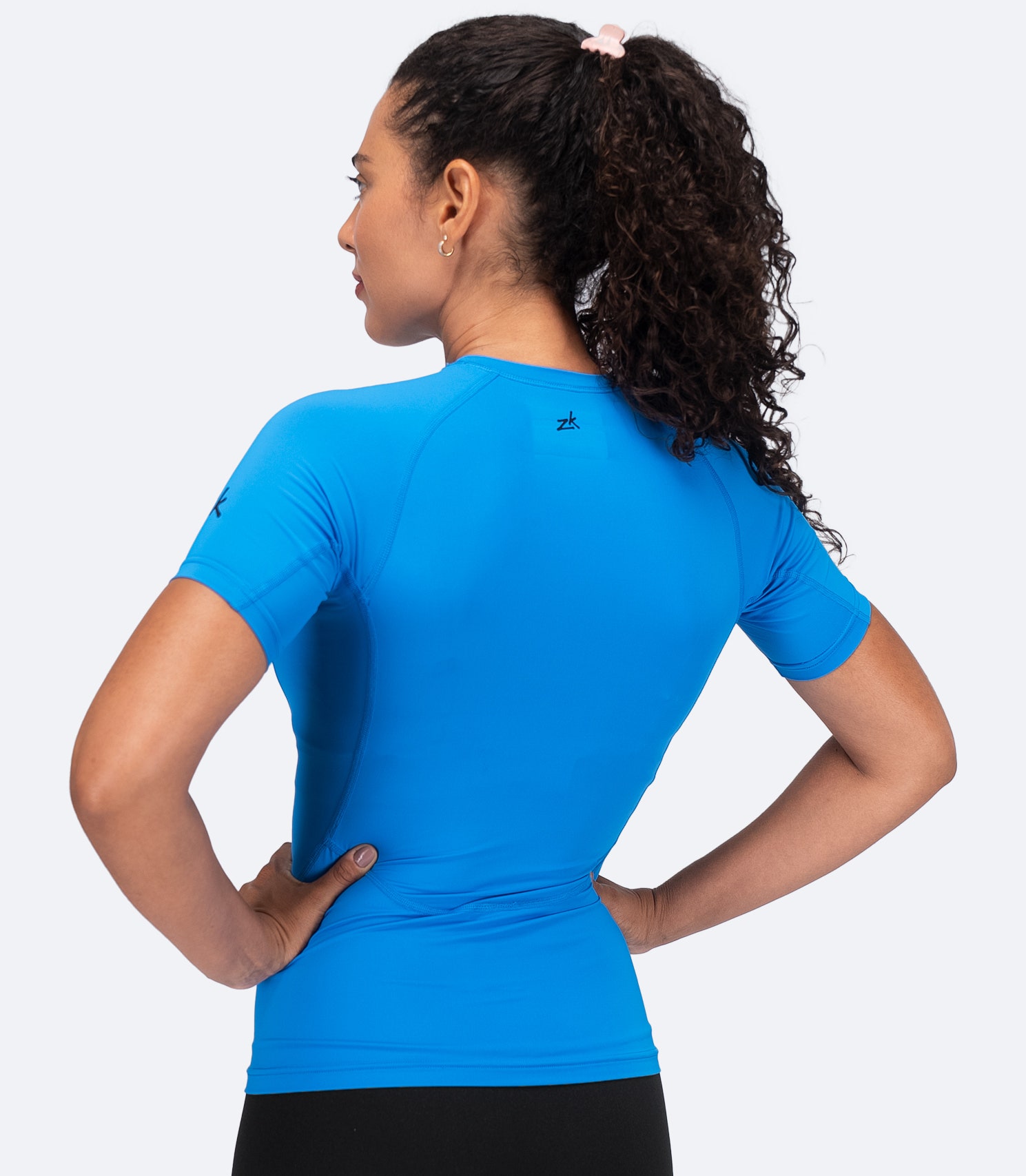 Back view of Zhik Women's Eco Spandex LT Top in Cyan with hands on hips, highlighting contoured fit and flatlock stitching.