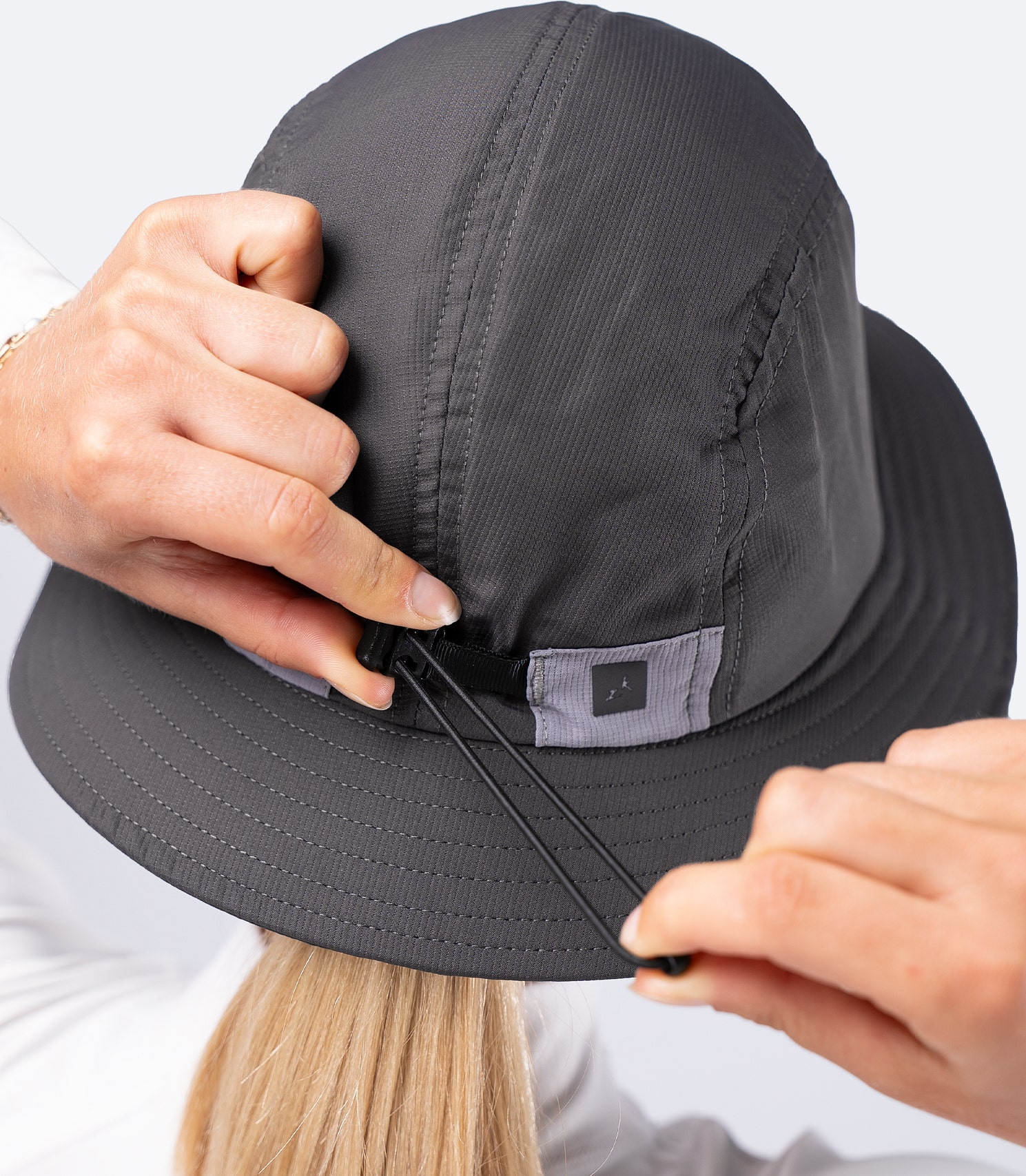Back view of Zhik Bucket Hat in Slate on female, holding rear elastic adjuster to tighten the fit in windy conditions