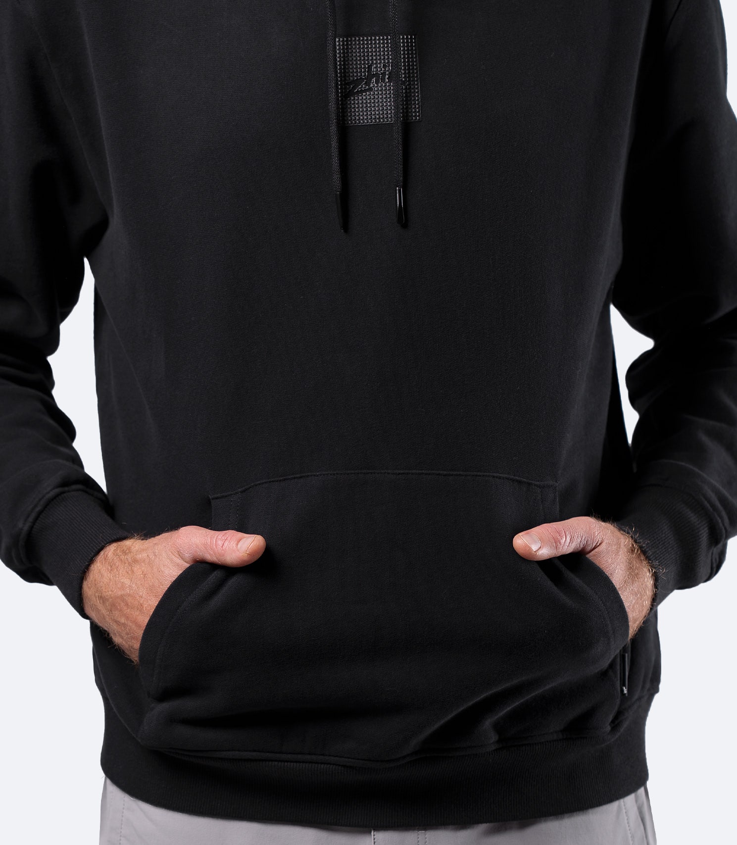 Close-up of black Zhik Men's Carbon Hoodie with hands in front pocket, showing soft brushed terry backing