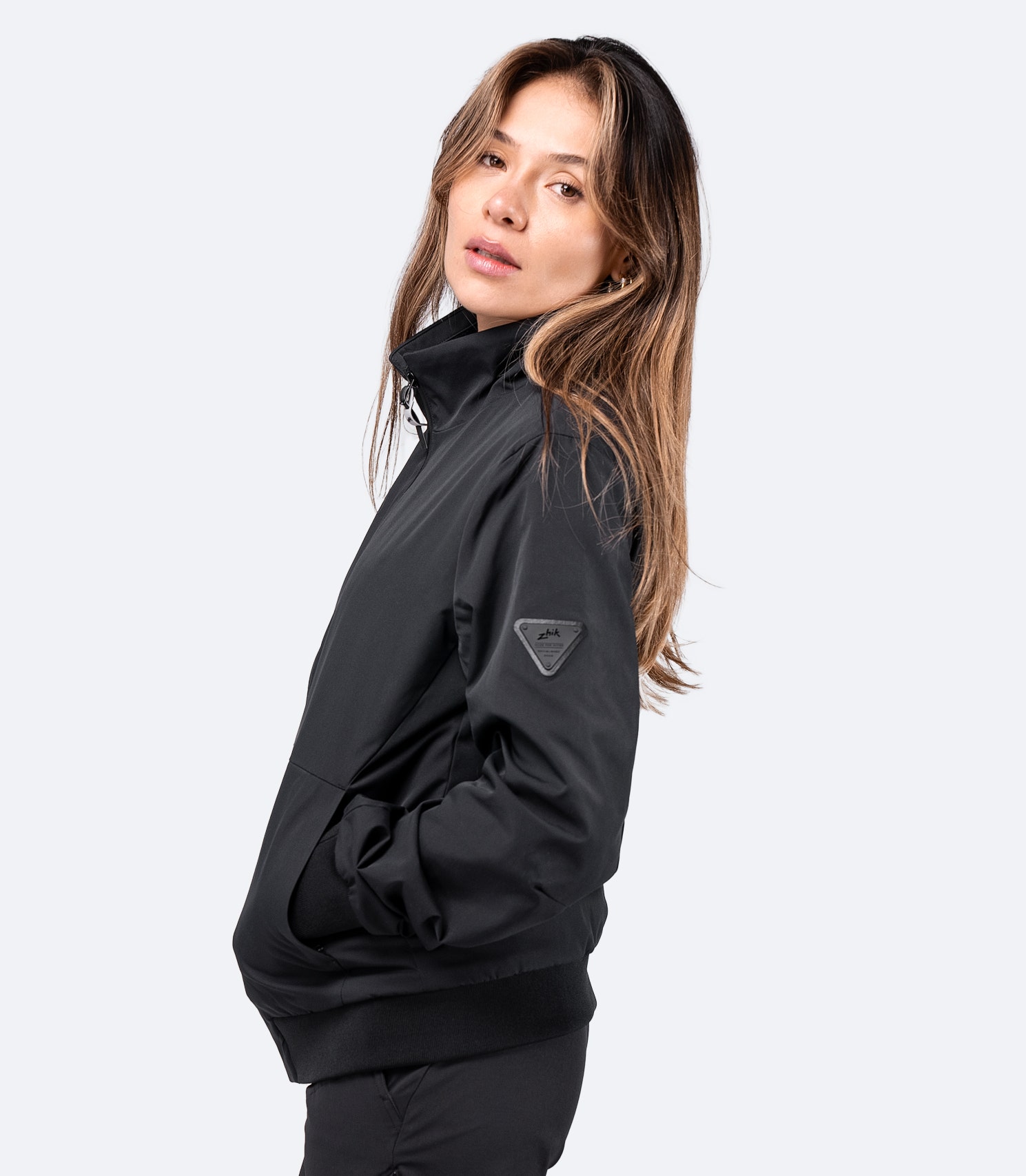 Side view of black Women's Flight Jacket by Zhik, showing smooth space-variant twill fabric and zippered pockets.