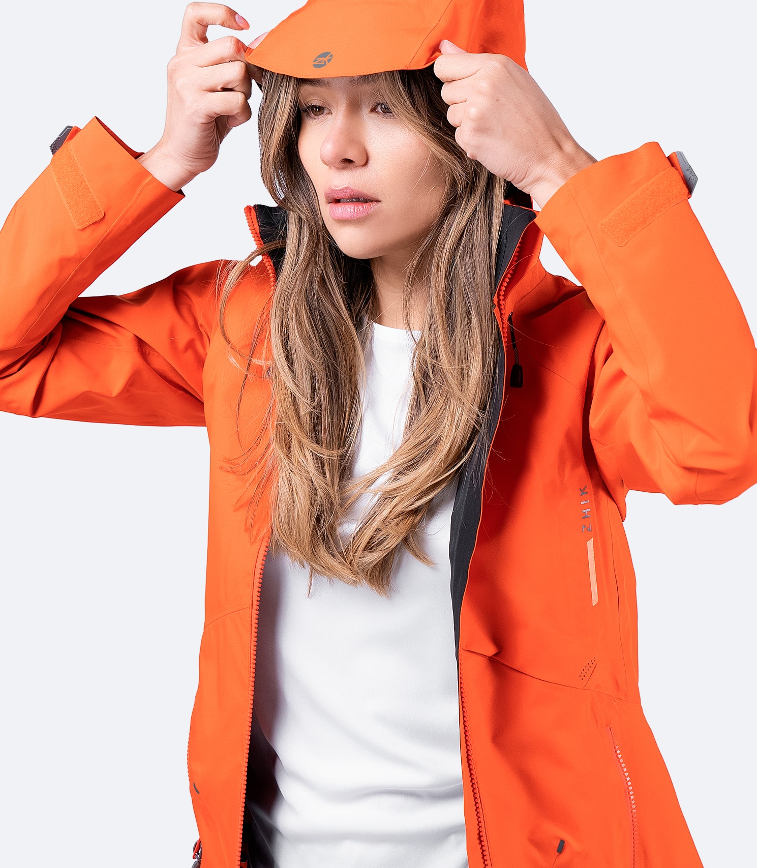 Zhik Women's Flame Red INS200 Jacket with hood up and chest zip open, showcasing breathable waterproof design and secure storage pocket