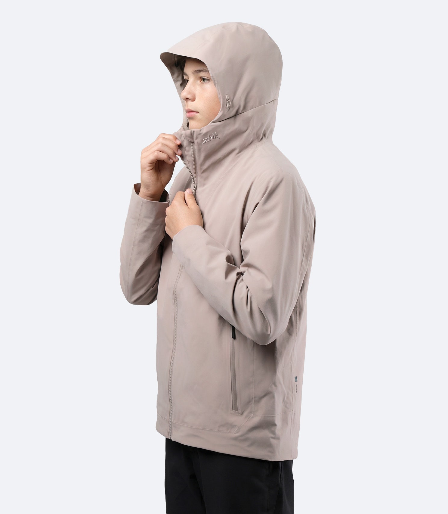 Vista lateral de la chaqueta Zhik Youth INS300 Inshore Active Jacket en color piedra con la capucha puesta, lista para condiciones costeras húmedas.