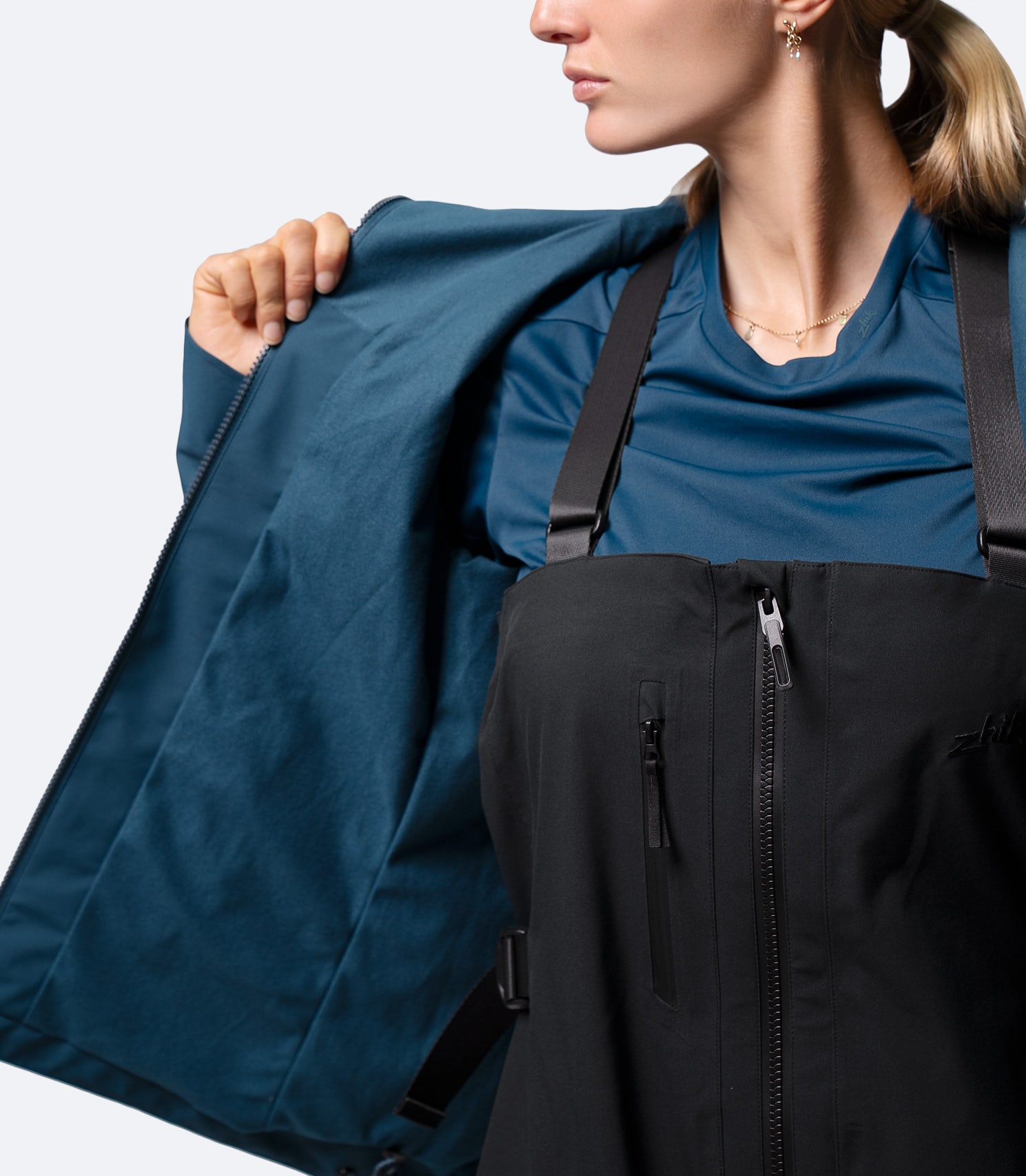Front view of Zhik INS300 Women's Inshore Active Jacket in Deep Teal, unzipped over salopettes for easy layering and movement