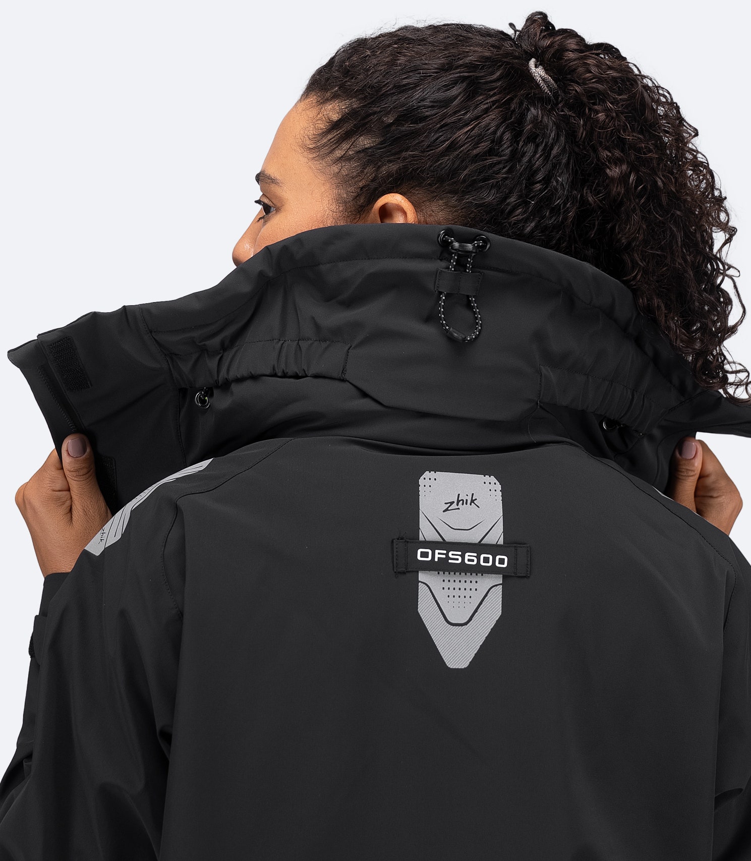 Rear close-up of Zhik black OFS600 Jacket with hood down, collar up, and extended back hem visible.