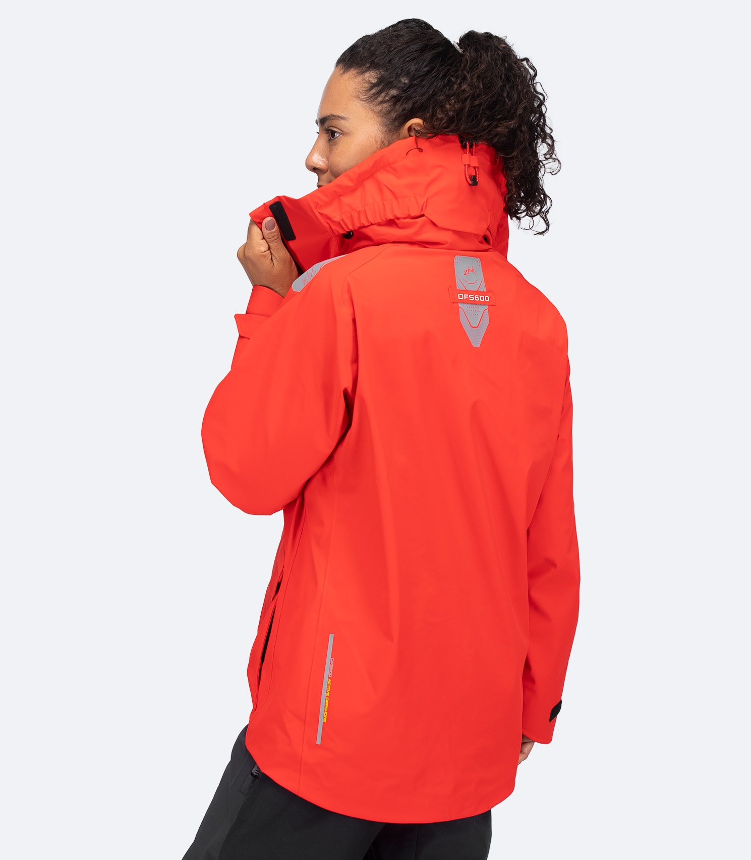 Rear view of Zhik Women's OFS600 Offshore Jacket in flame red, collar raised, showing ergonomic fit and stowed hood.