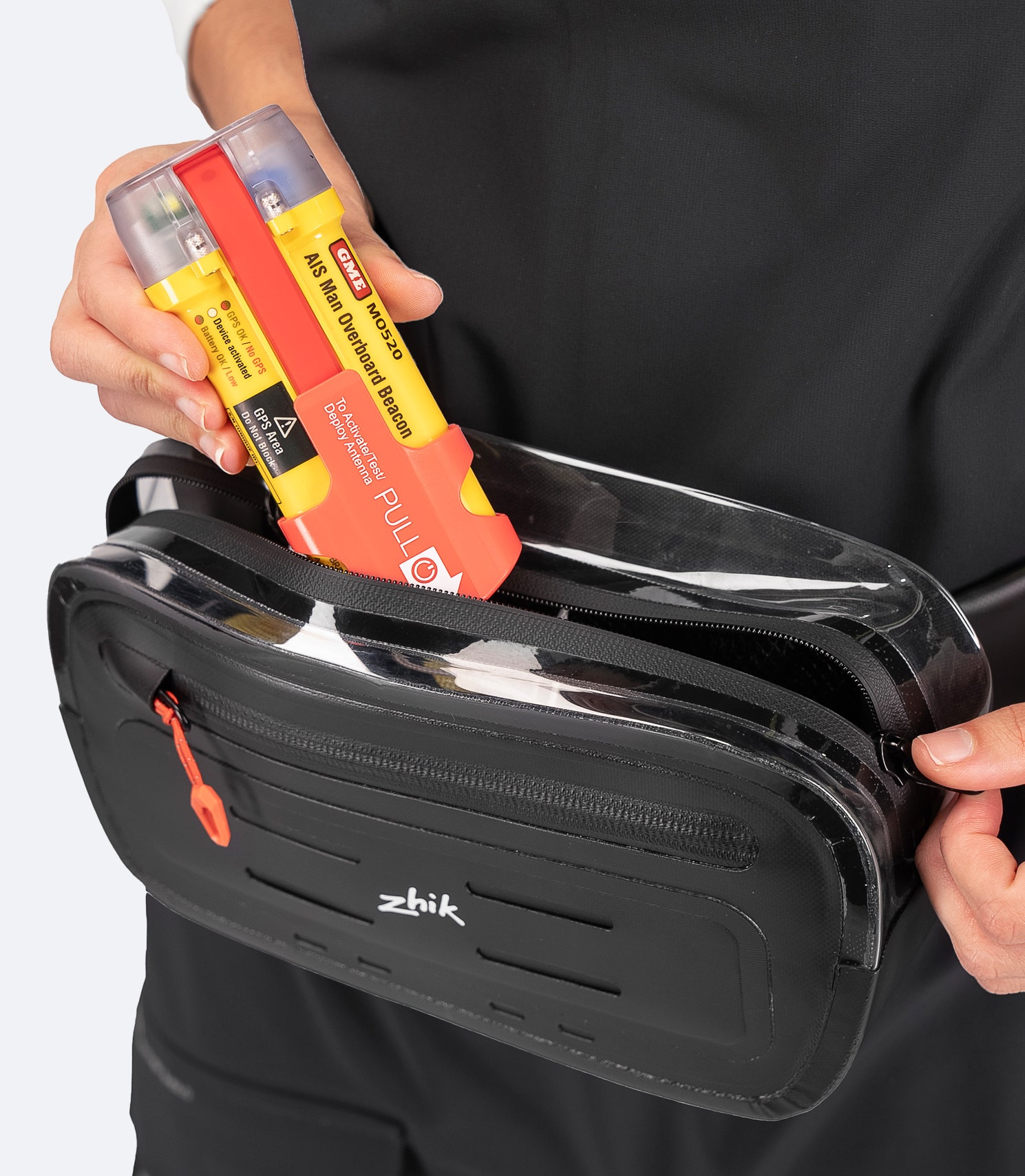 Close-up of black Zhik Storm Sling Waist Pack open, with AIS beacon in drainage pocket and view of waterproof main compartment and internal bungee loop.