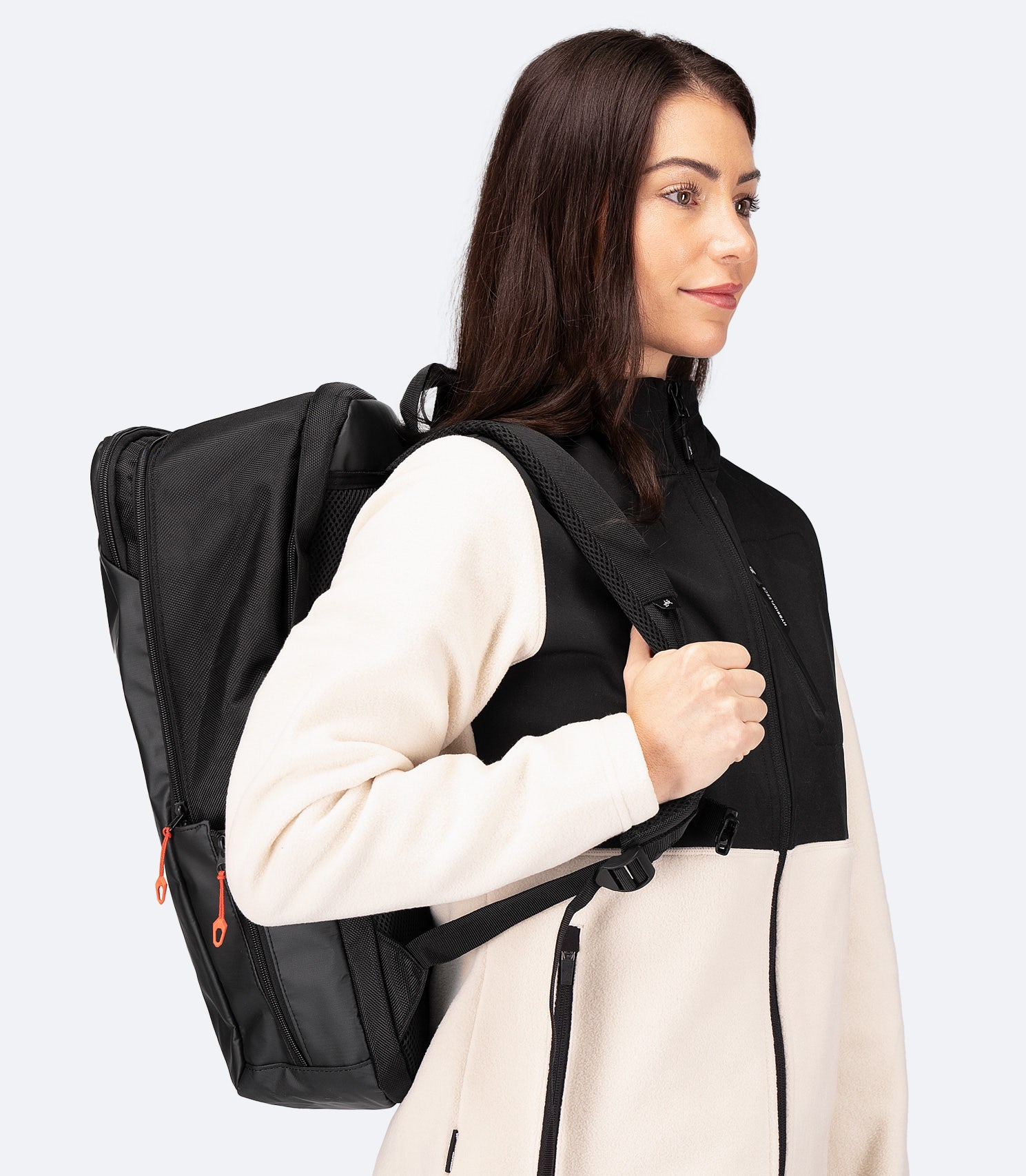 Side view of model wearing Zhik 25L Team Backpack in black, highlighting deep front pocket, adjustable side bottle holder, and ergonomic fit
