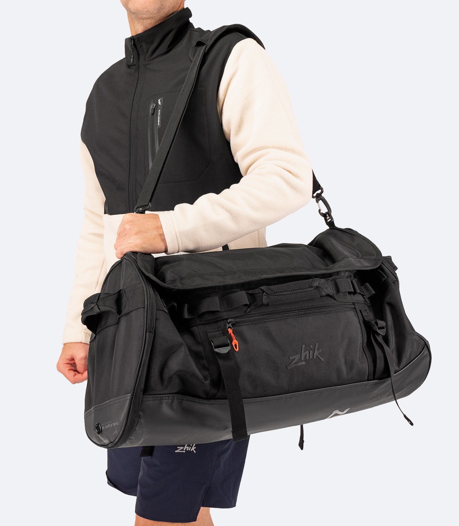 Model carrying the Zhik 55L Duffel Bag in black from the side, showing haul handles, durable construction, and external compression straps