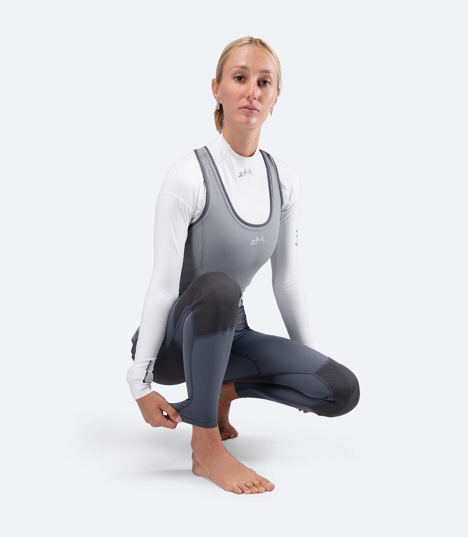 Zhik Women's Hybrid Gear Performance Skiff Suit in grey shown crouched, highlighting stretch mobility and body-mapped comfort