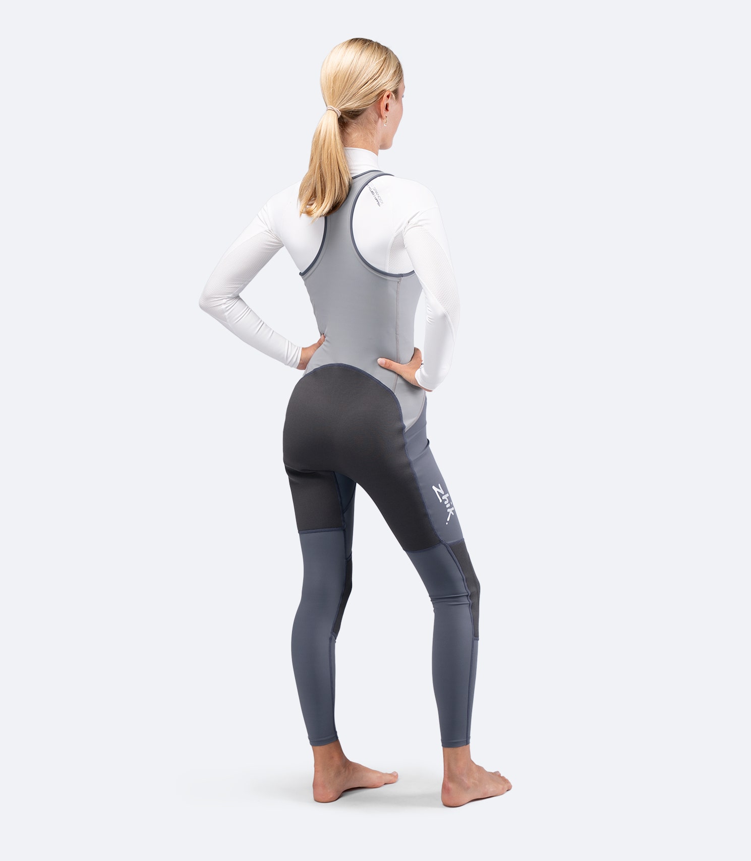 Rear view of Zhik Women's Hybrid Gear Performance Skiff Suit in grey, hands on hips, showing racerback straps and fit