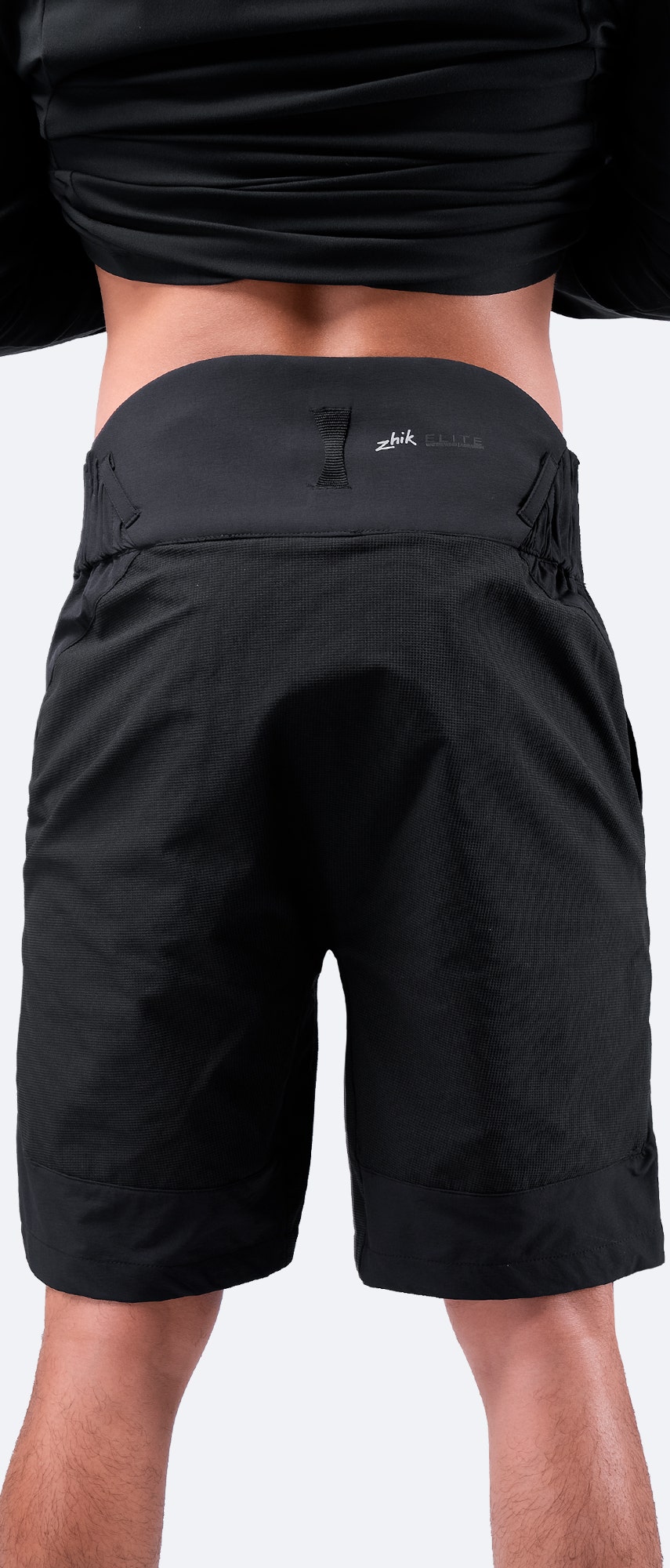 Vista posterior de los pantalones cortos Elite negros para hombre de Zhik, que cuentan con un panel trasero alto para protección lumbar y un lazo de secado característico.
