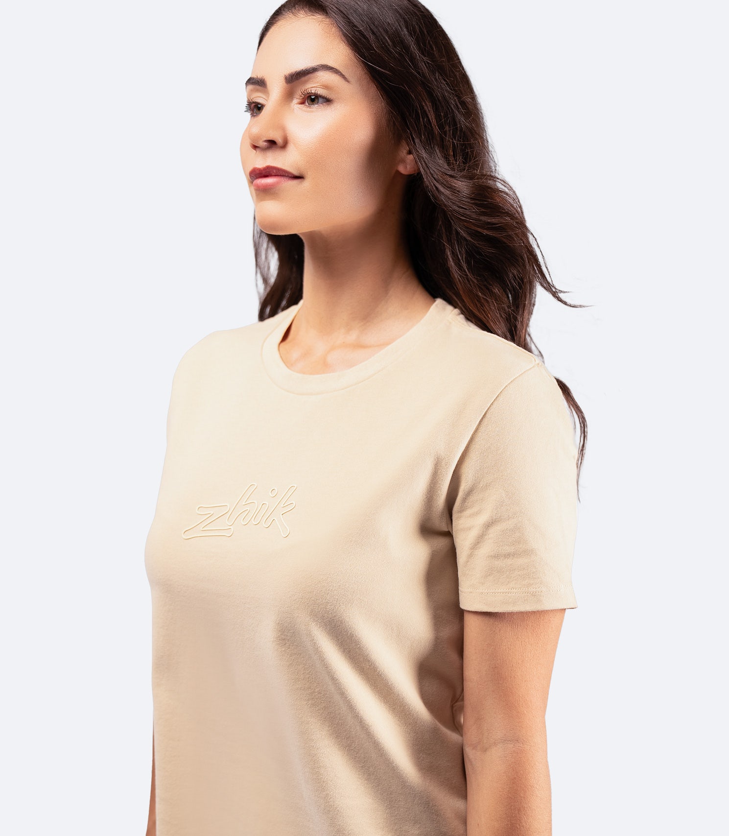 Side-angle shot of Women's Zhik Logo T-Shirt in sand, featuring a relaxed cropped fit and durable cotton construction.