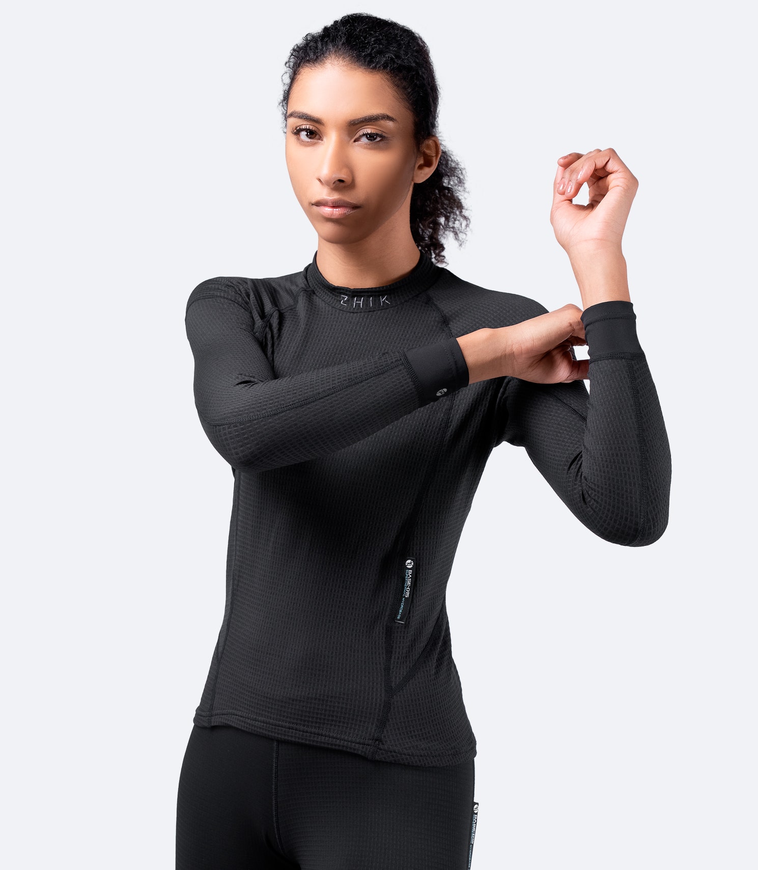 Black Zhik Superthermal™ Hydrobase® Top, female model front view, highlighting high-stretch sleeves and breathable thermal fabric.