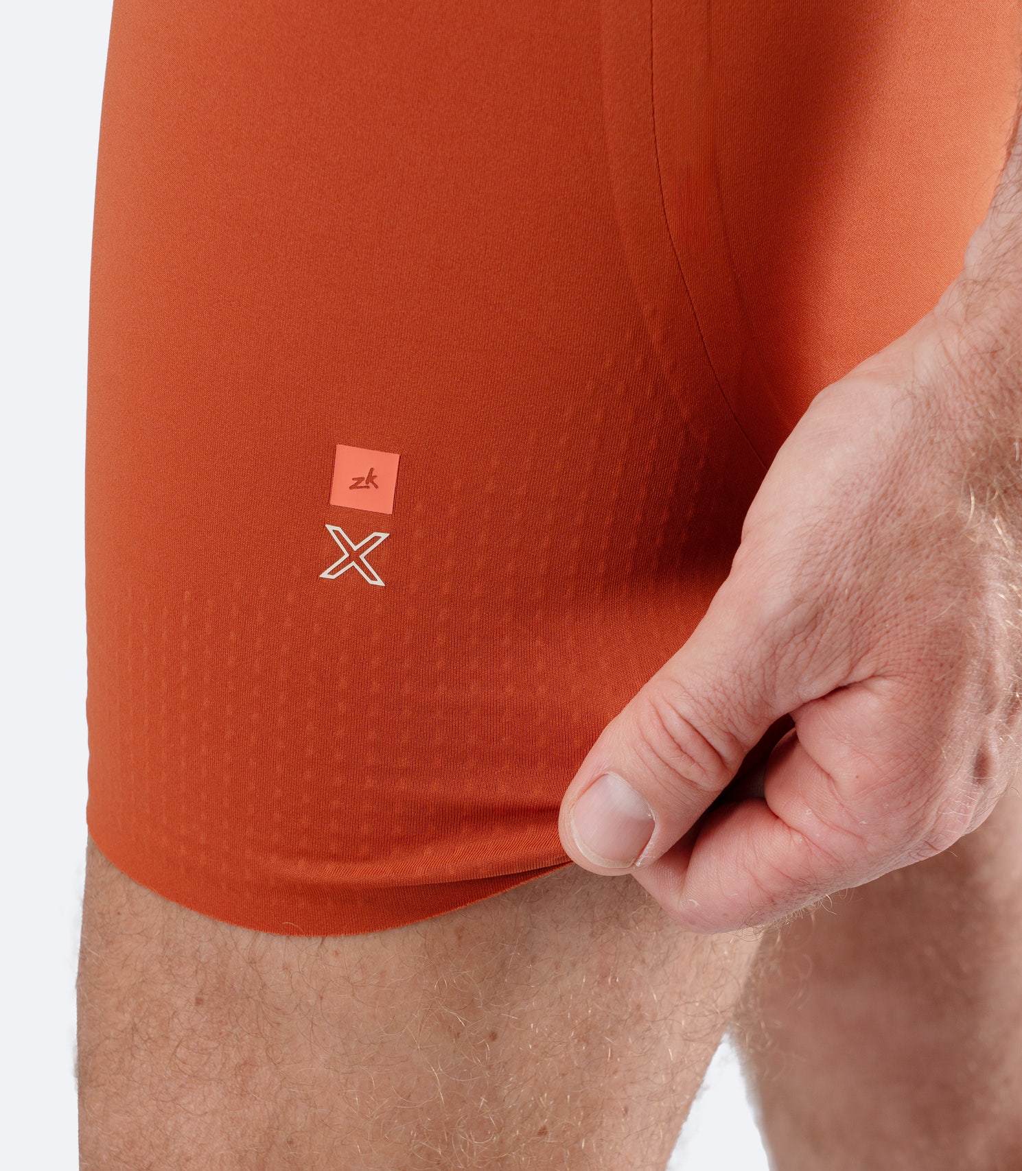 Close-up of Zhik Men’s X Unisuit in Red Earth with hand stretching graphene-infused leg fabric.