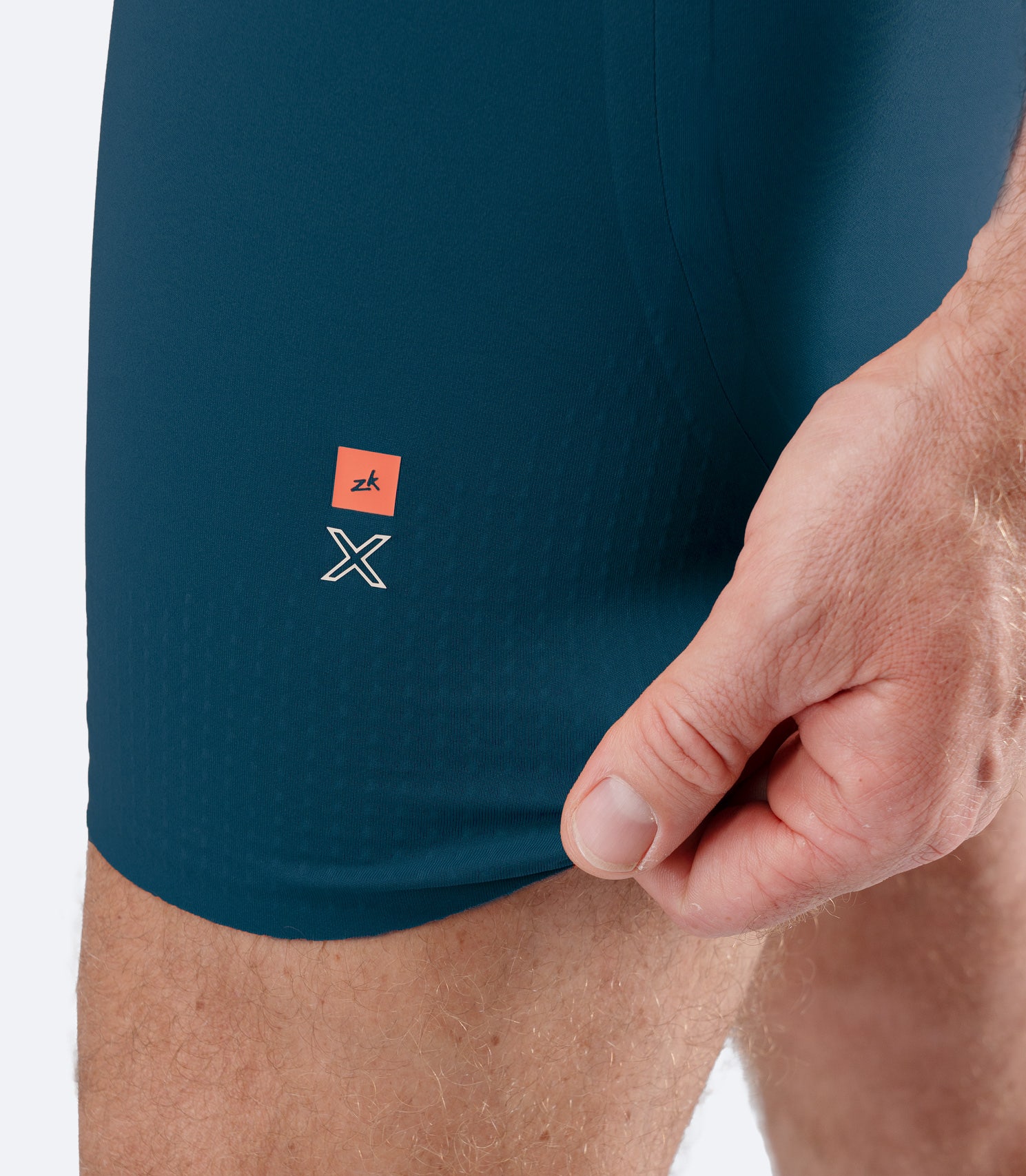 Close-up of Zhik Men’s X Unisuit in Deeo Teal with hand stretching graphene-infused leg fabric.