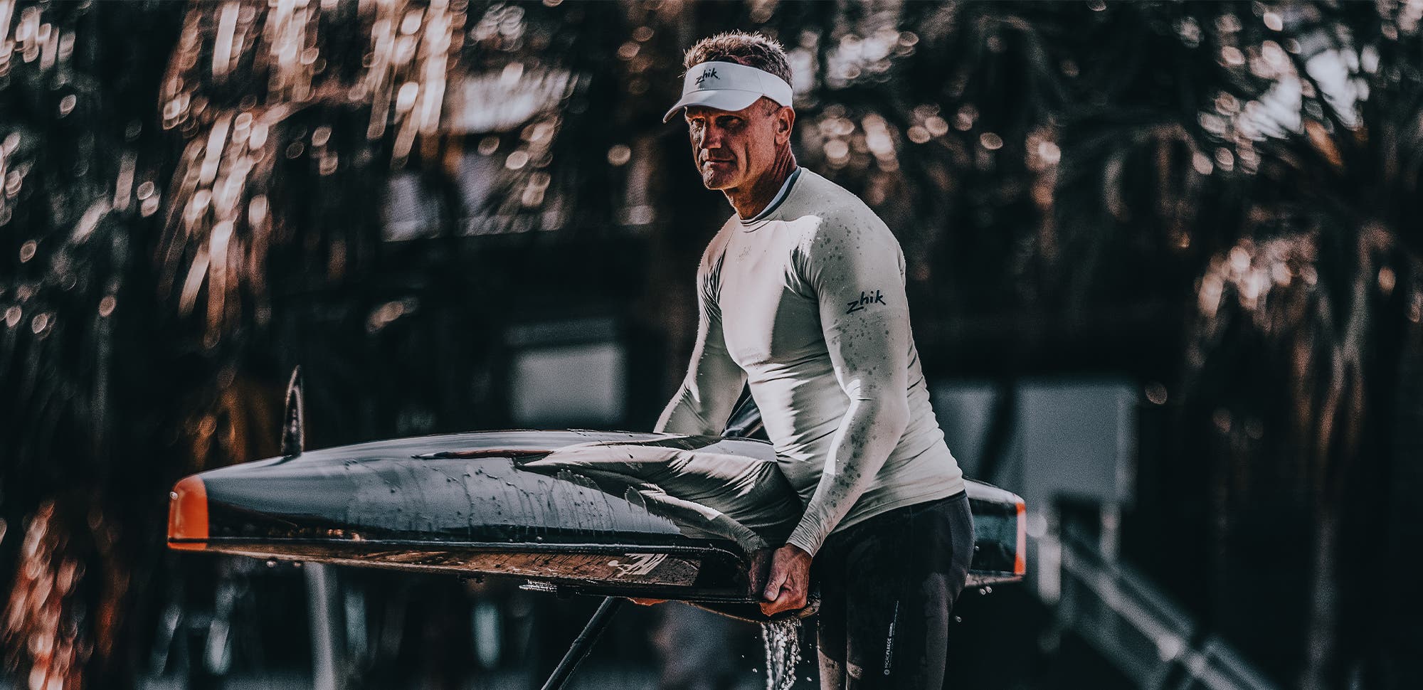 Paddle athlete washing their surf ski on the grass wearing Zhik high-performance sun protection gear.